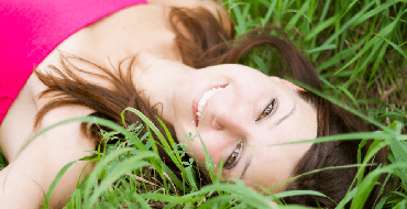 Smiling woman with healthy white teeth laying down in green grass Great Lakes Family Dental Group